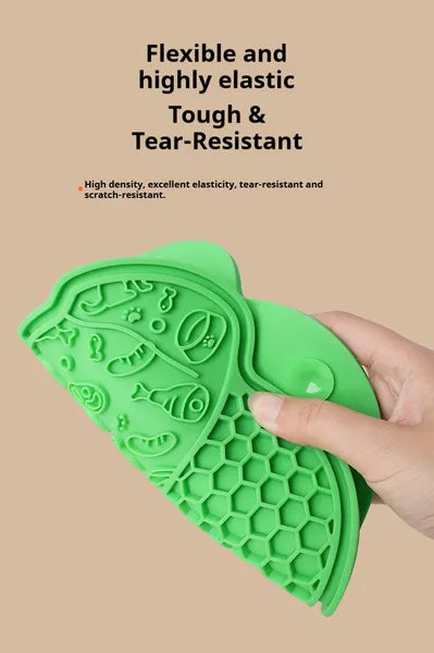 Green silicone pet licking mat with fish designs held by a hand on a beige background
